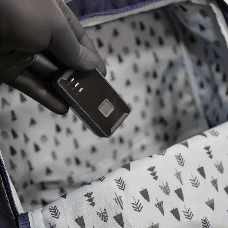 Texte alternatif : Une personne portant un gant nitrile noir tenant un appareil Trackd noir à l'intérieur du compartiment ouvert d'un sac à dos bleu avec une doublure à motifs.