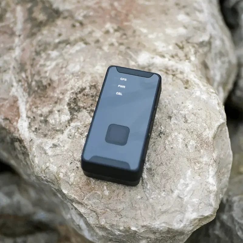 Un traceur électronique noir rectangulaire avec des étiquettes d’état reposant sur la surface plane d’une grande roche texturée de couleur claire.