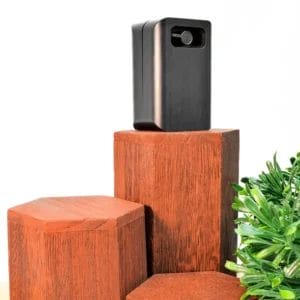 Compact black Trackd electronic device placed on hexagonal wooden pedestals with a green plant.