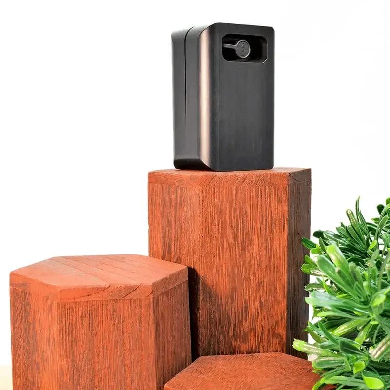 Compact black Trackd electronic device placed on hexagonal wooden pedestals with a green plant.