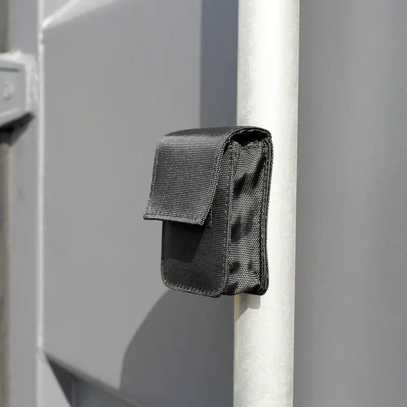 Une pochette de protection en nylon noir fixée verticalement à un tuyau métallique gris sur un fond industriel gris assorti.